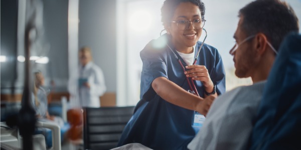 A registered nurse listening to a patient's heartbeat in a hospital bed.