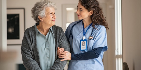 A patient care technician helping a patient talk a walk.