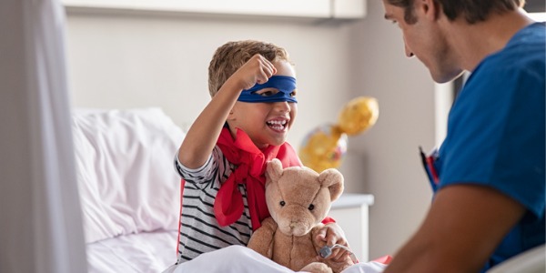 A pediatric nurse having fun with a young male patient on his hospital bed.