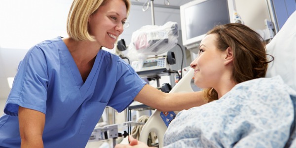 A medical-surgical registered nurse smiling with a patient in a hospital bed.