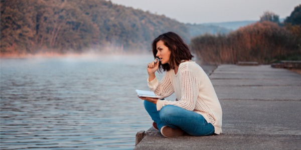 A fiction writer jotting down some thoughts for her book while sitting on a dock.