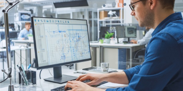 An industrial architect working with CAD software on a desktop computer.
