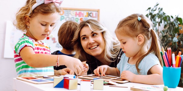 A preschool teacher helping young children with puzzles.
