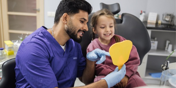 A pediatric dentist showing a young patient her teeth with the use of a mirror.