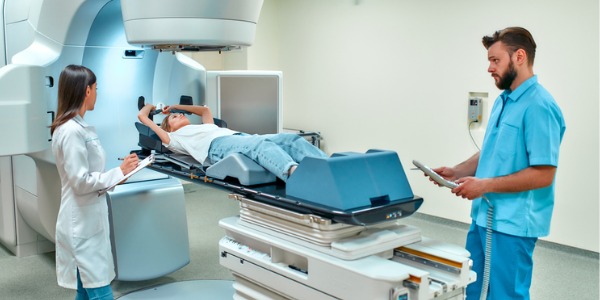 Two radiation therapists giving radiation therapy to a female patient.