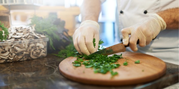 A food preparation worker chopping up vegetables on a cutting board.
