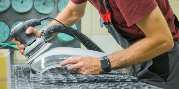 A hand polishing worker using a polishing machine on a car part.
