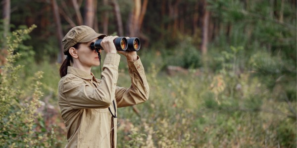 A female park ranger monitoring the park through binoculars.