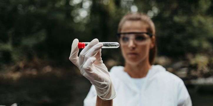 An environmental technician taking a water sample outside.