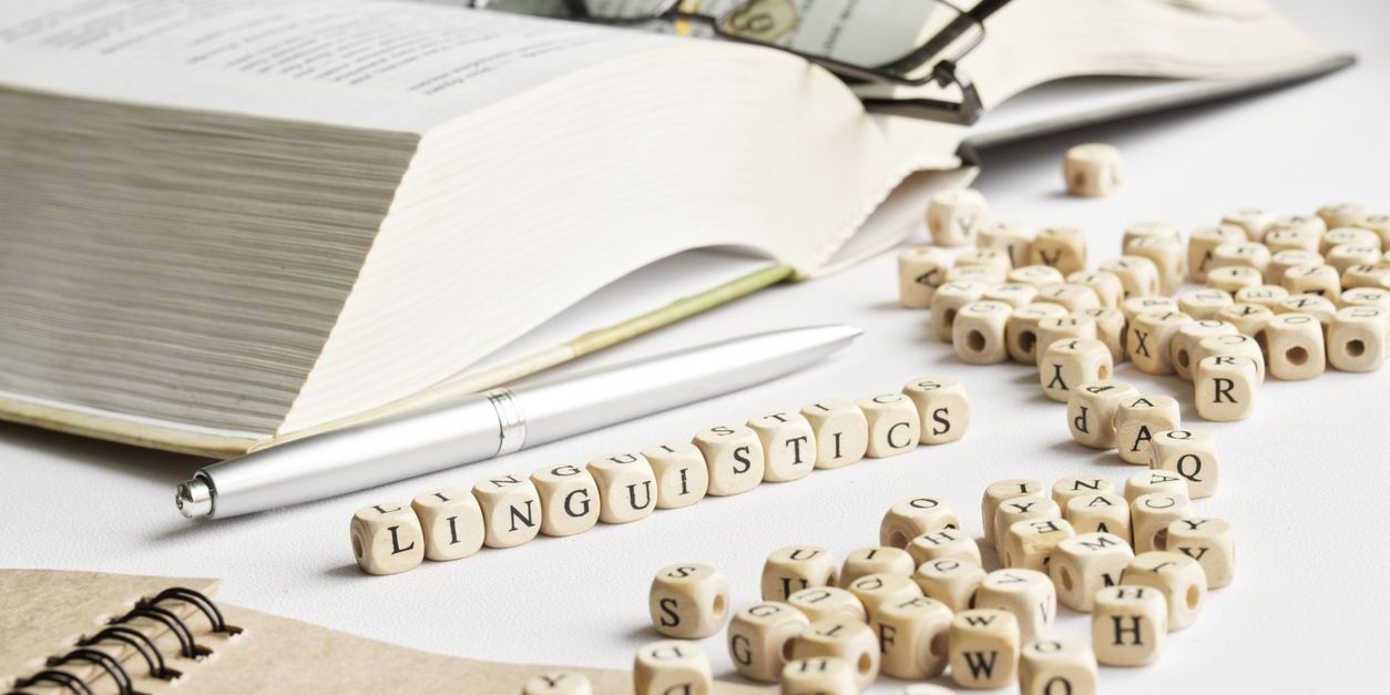 Word linguistics next to open book, glasses, notepad, and pen. Depicting a linguist studying.