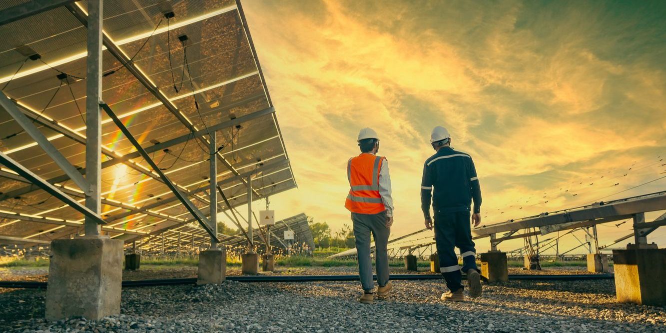 A renewable energy engineer walks with a colleague through a field of solar panels.