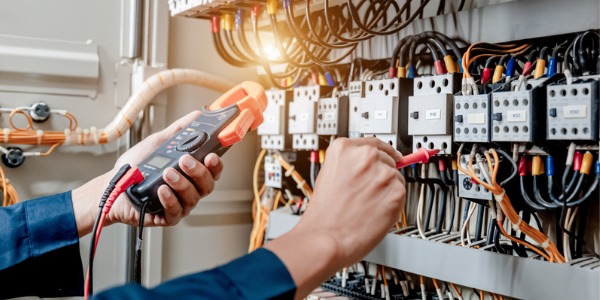 An electrical technician using a multimeter to test the electrical installation in an electrical system control cabinet.