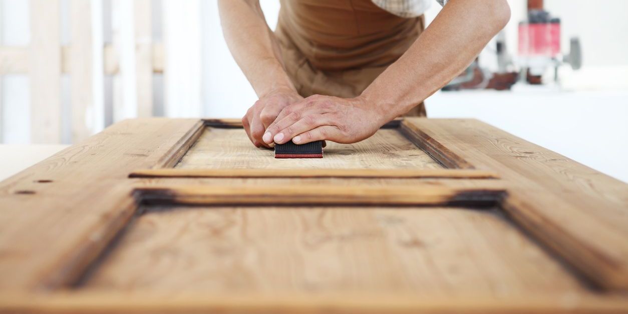 A furniture maker finishing off a cabinet door with sandpaper.