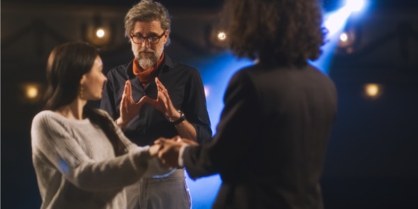 A theatrical director guiding two actors on stage.