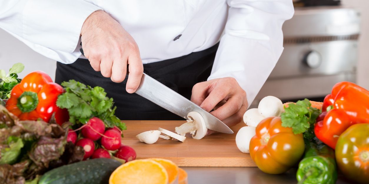 A vegetable chef cutting up vegetables in a professional kitchen.