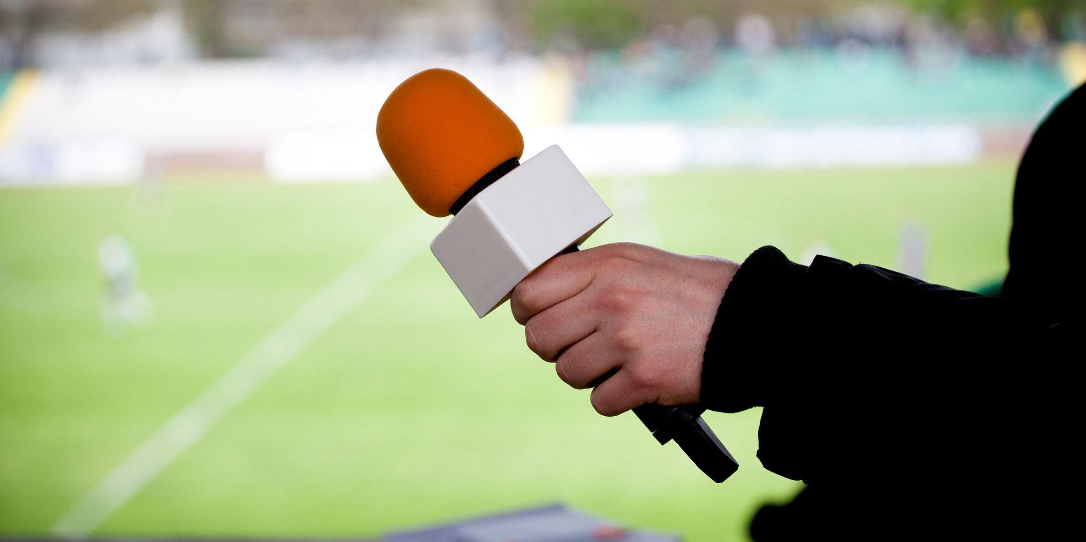 A hand holding a microphone for interview during a football match.
