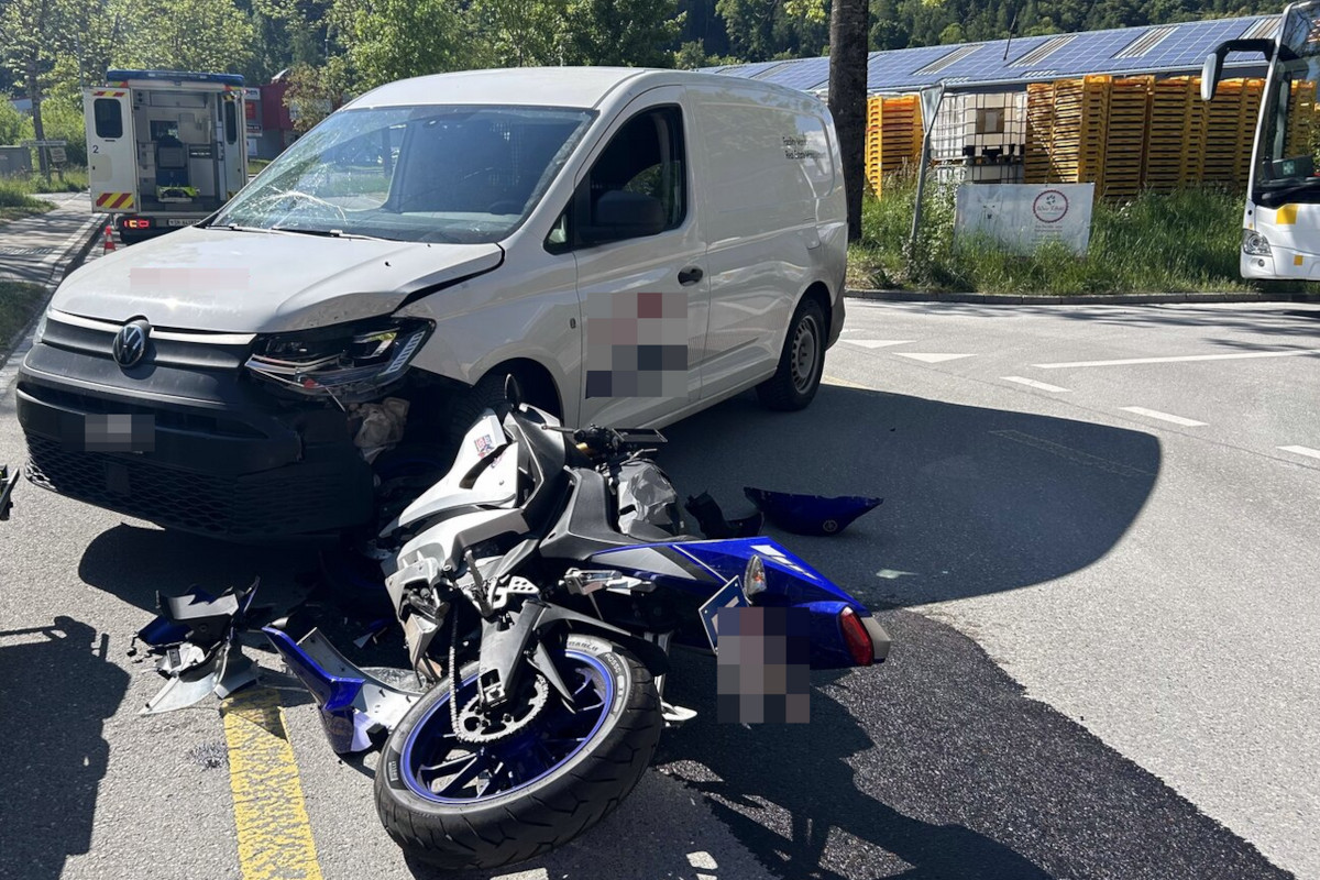 Auf dem Bild ist ein Unfall zwischen einem weißen Van und einem blau-silbernen Motorrad auf einer Straße zu sehen. Der Van steht nahe an einem beschädigten Motorrad, umgeben von Trümmern.