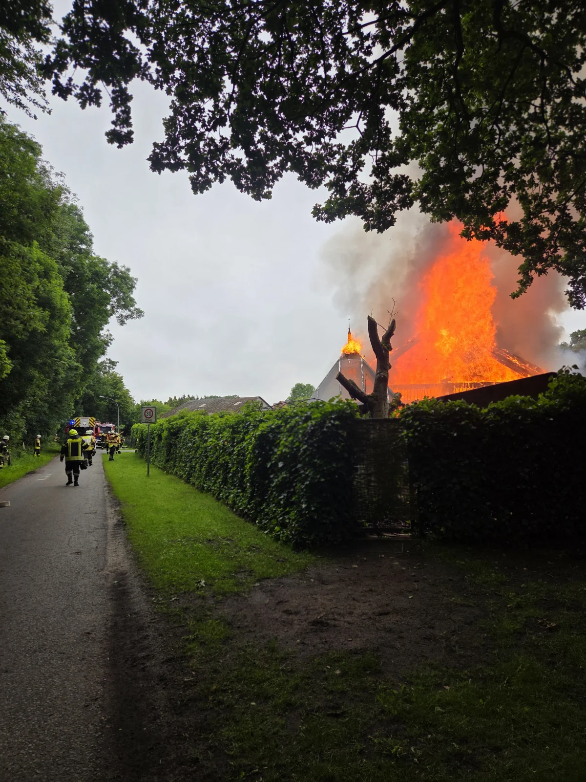 Ein Dachstuhl steht in Flammen, während Feuerwehrleute versuchen, das Feuer zu löschen. Dicker Rauch steigt in den Himmel auf.