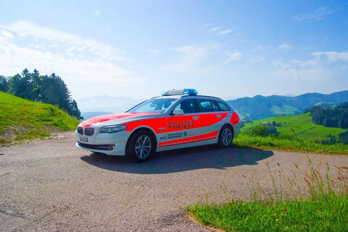 Ein Polizeifahrzeug der Kantonspolizei St. Gallen steht auf einer ländlichen Straße mit grünen Hügeln im Hintergrund. Der Himmel ist blau und klar.