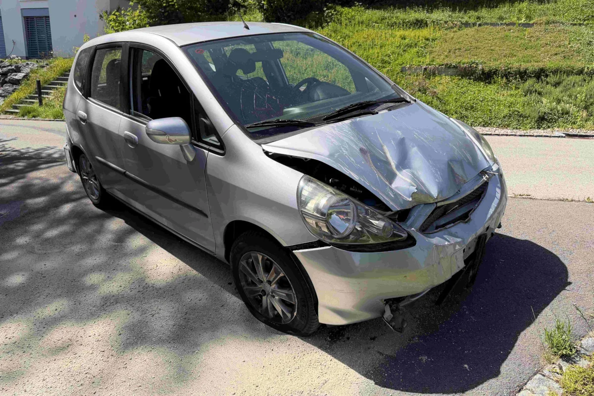 Ein silbernes Auto mit deutlichen Schäden an der Front steht auf einer asphaltierten Straße. Die Motorhaube ist stark eingedrückt.