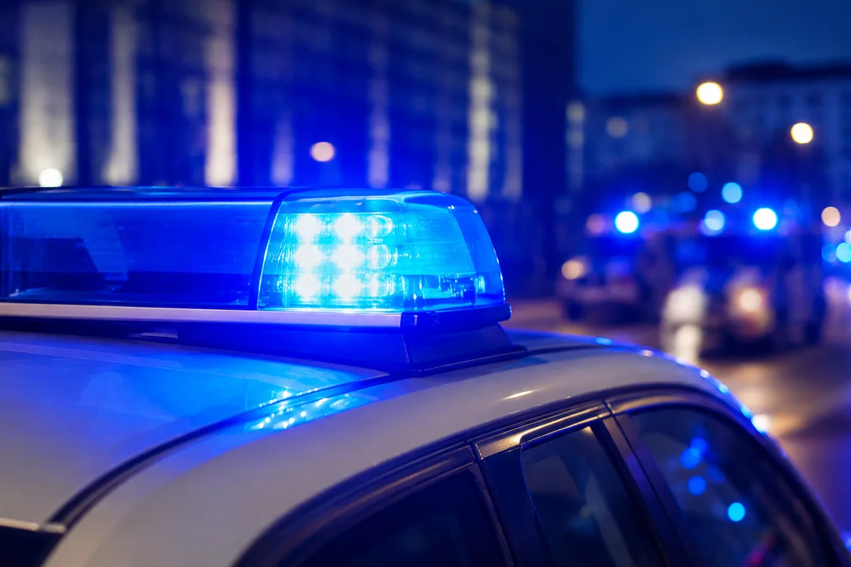 Ein blaues Polizeilicht leuchtet auf dem Dach eines Einsatzfahrzeugs. Im Hintergrund sind weitere beleuchtete Fahrzeuge erkennbar.