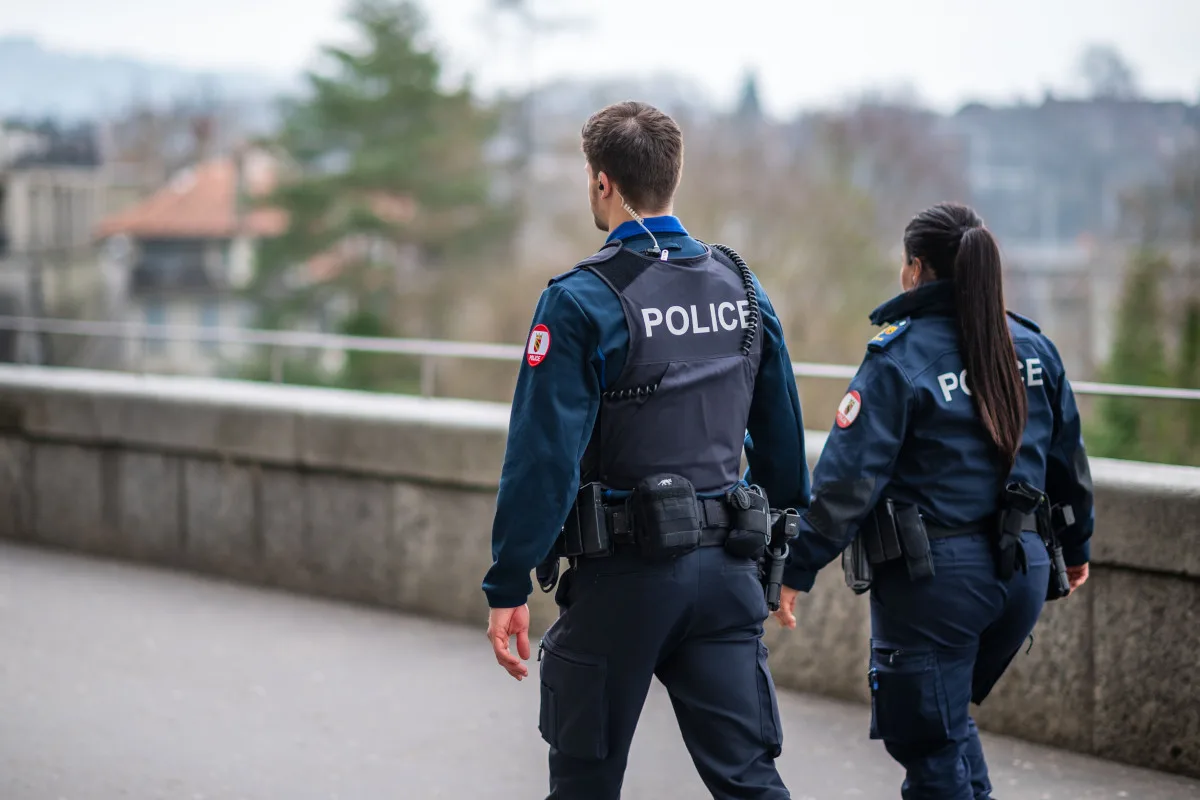 Zwei Polizisten in Dunkelblau sind auf einer Straße unterwegs. Die Umgebung wirkt urban mit unscharfem Hintergrund.