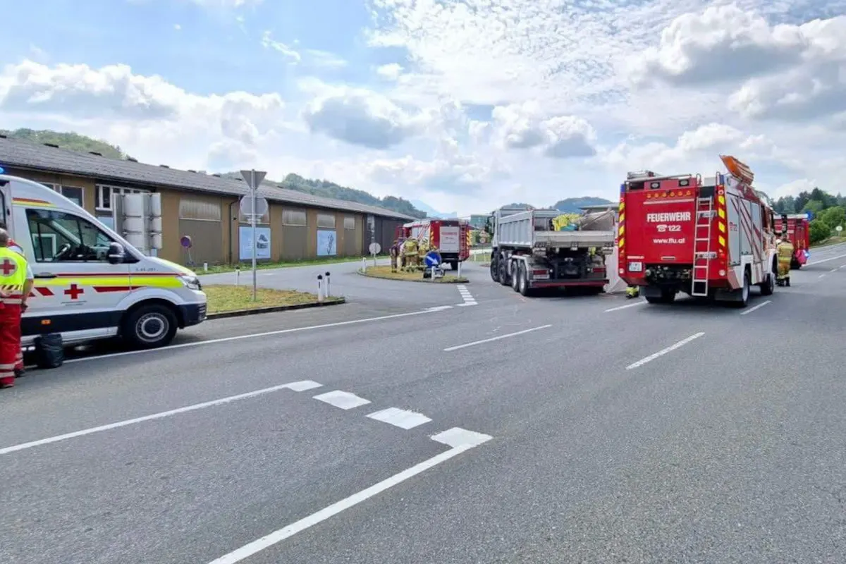 Ein Feuerwehrfahrzeug und ein Rettungswagen sind bei einem Einsatz auf einer Straße vor einem Gebäude zu sehen. Ein Lkw steht ebenfalls auf der Straße, umgeben von Einsatzkräften.