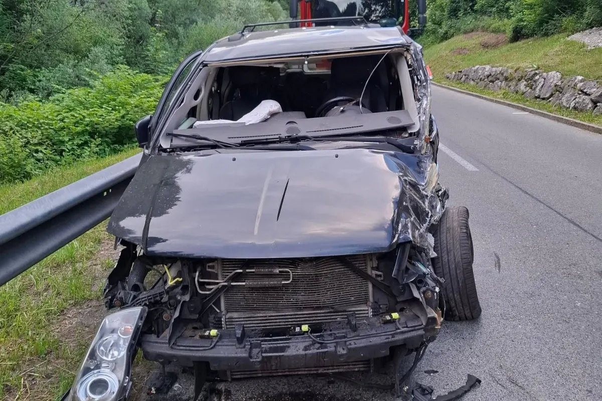 Ein schwarzes Auto steht mit beschädigter Frontpartie auf einer Landstraße. Im Hintergrund ist ein Feuerwehrfahrzeug erkennbar.