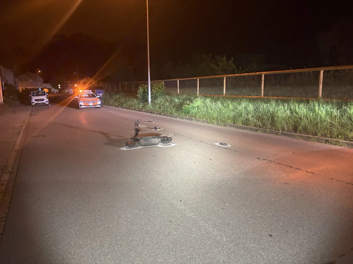 Bei Nachtaufnahme liegt ein E-Scooter auf der Straße. Im Hintergrund sind Polizeifahrzeuge mit eingeschaltetem Blaulicht sichtbar.