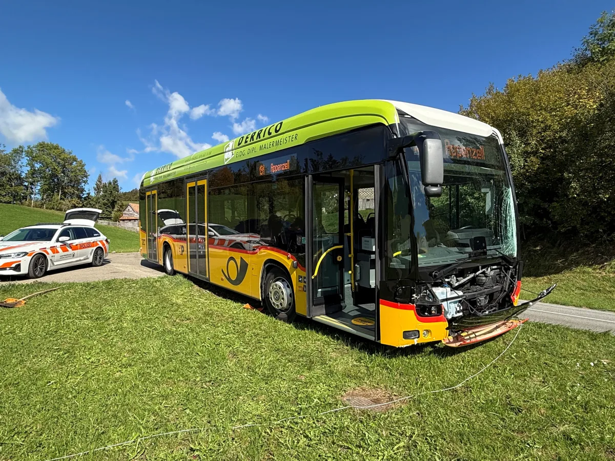 Ein Bus mit deutlich sichtbarem Frontschaden steht auf einer Wiese, daneben ein Einsatzfahrzeug der Polizei.