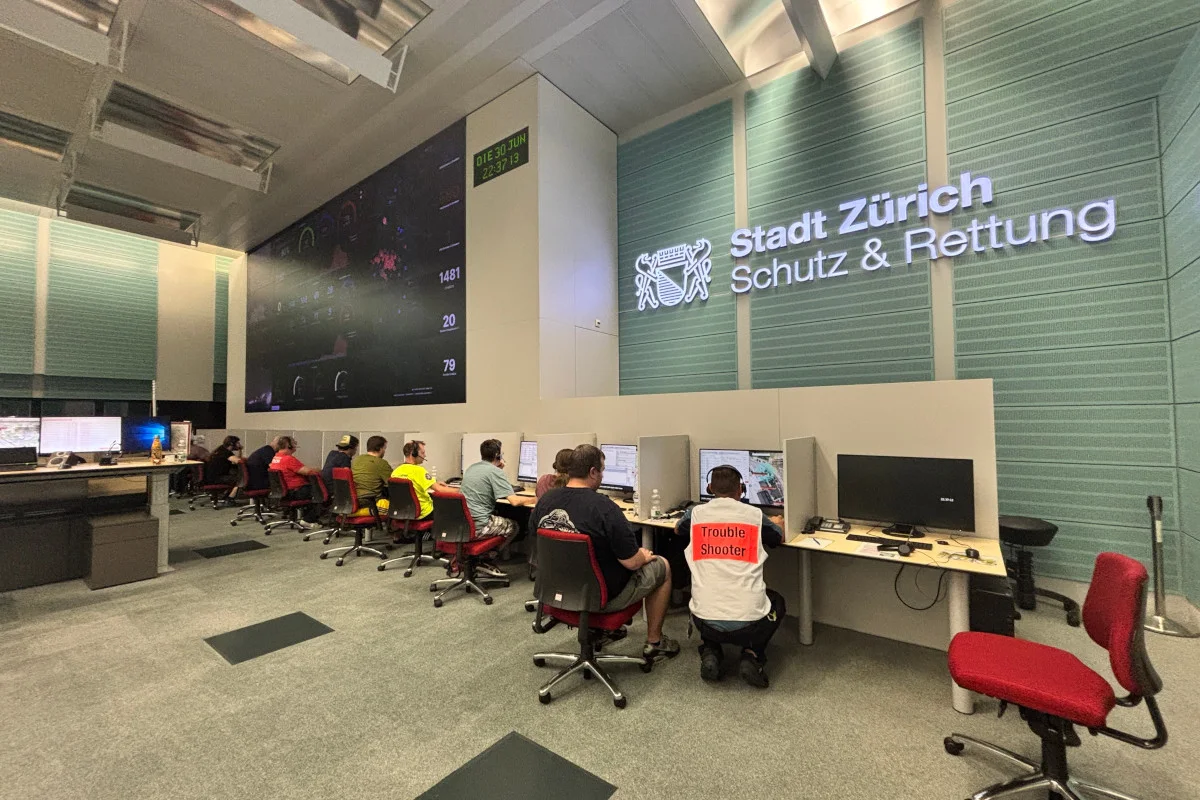 In einem großen Raum mit Bildschirmen an den Wänden arbeiten mehrere Personen an Computern unter dem Schild 'Stadt Zürich Schutz & Rettung'.