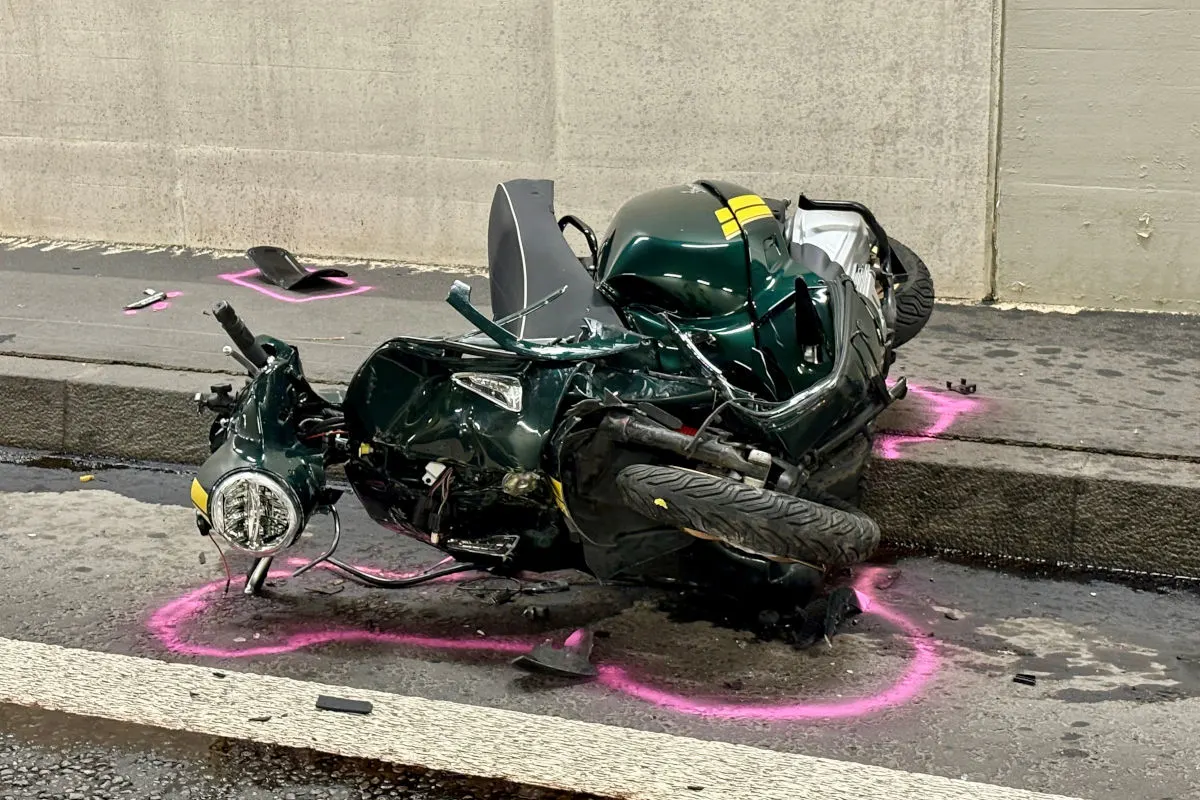 Ein beschädigtes Motorrad liegt auf der Straße, umgeben von Trümmern und Farbspray-Markierungen auf dem Asphalt. Teile des Fahrzeugs sind abgebrochen.