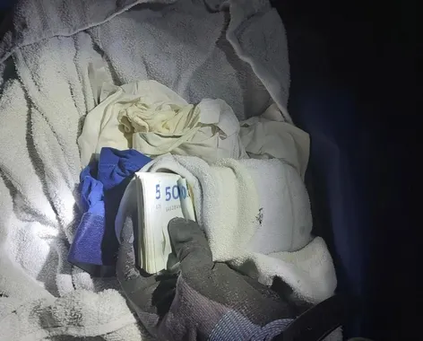 Ein Bündel von Geldscheinen liegt umgeben von Handtüchern und Kleidungsstücken in einem dunklen Behälter.