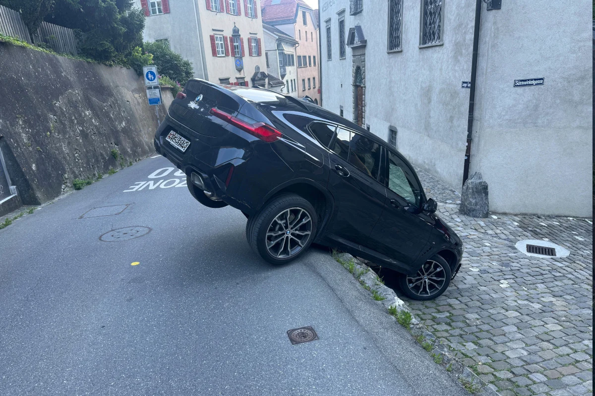 Ein schwarzer BMW steckt mit dem Heck in einer engen Straße fest und neigt sich nach hinten in eine Grube.