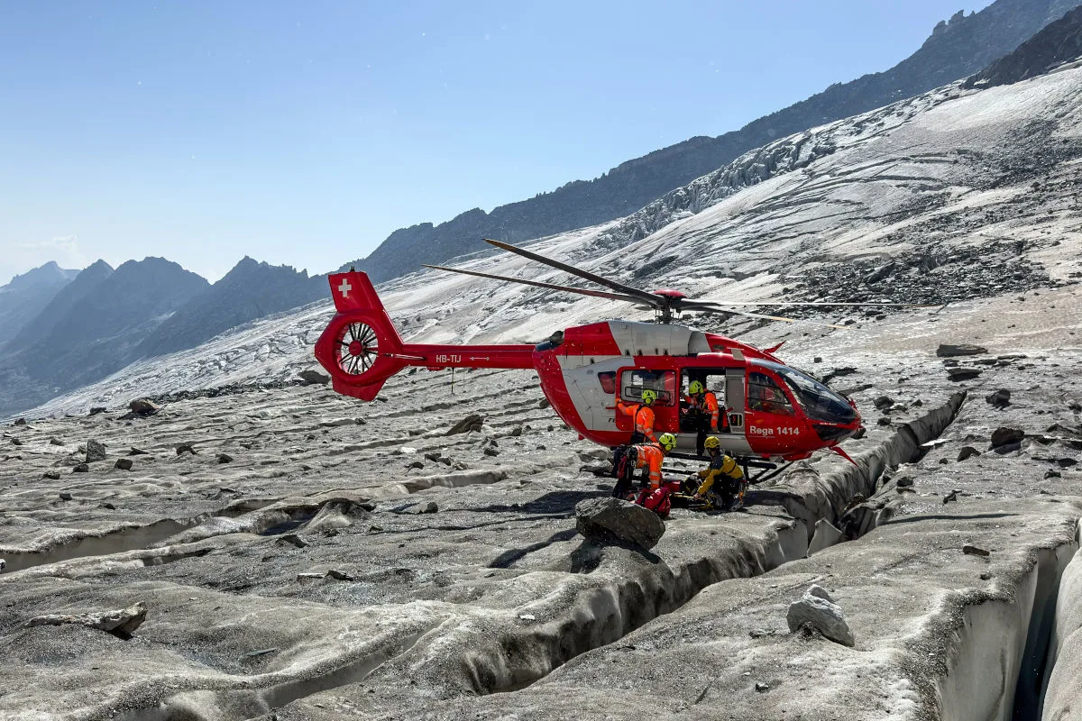 Ein roter Rettungshubschrauber der Rega steht auf einem Gletscher. Einsatzkräfte in orangenen Anzügen sind um den Hubschrauber herum aktiv.