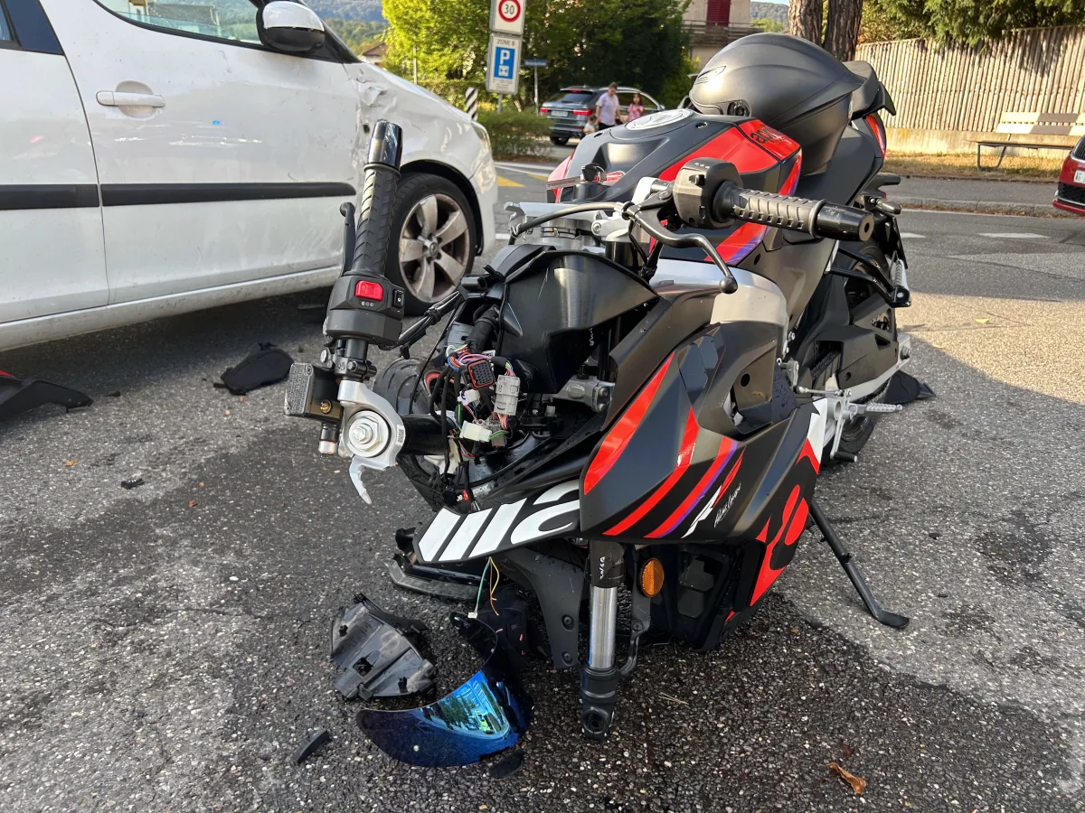 Ein beschädigtes Motorrad steht vor einem weißen Auto, beide zeigen Unfallspuren und Schäden auf der Straße.