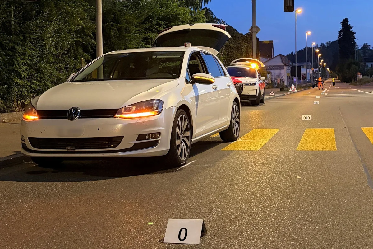 Ein weißer VW mit offenem Kofferraum steht auf einer beleuchteten Straße in der Nacht. Im Hintergrund ist ein Polizeiauto zu sehen.