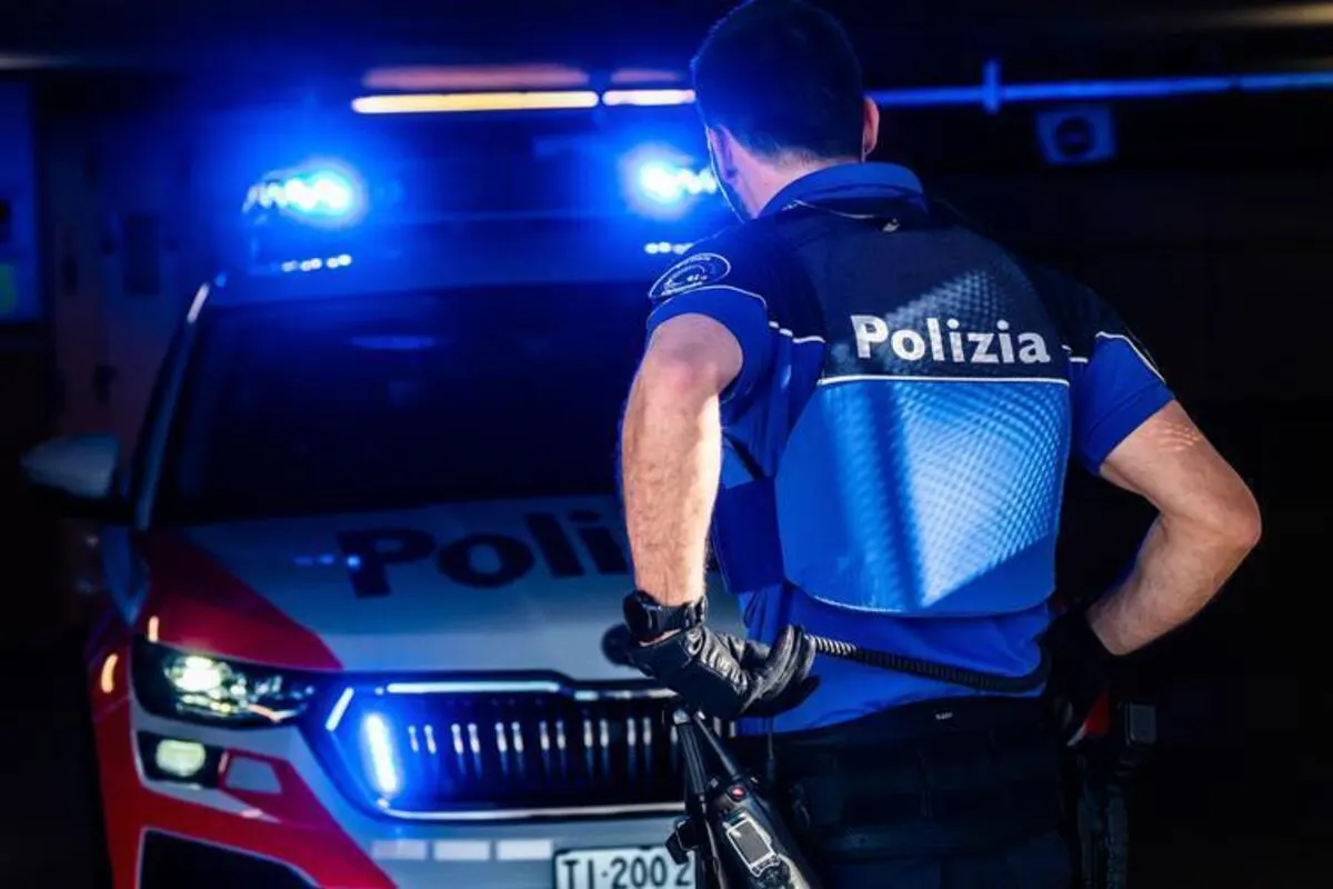 Ein Polizist steht mit dem Rücken zur Kamera vor einem Polizeiauto mit eingeschaltetem Blaulicht. Das Fahrzeug hat eine sichtbare Beschriftung.