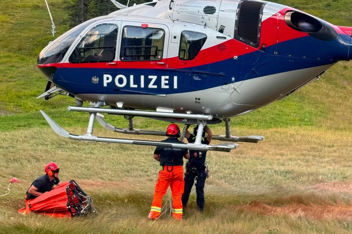 Ein Polizeihubschrauber steht mit Personal auf einer Wiese. Zwei Personen arbeiten am Hubschrauber.