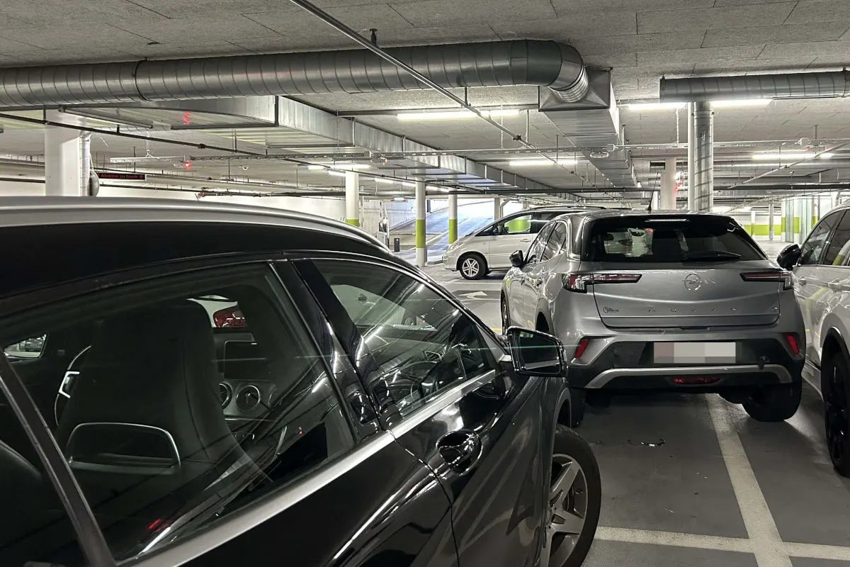 Eine Tiefgarage mit mehreren eng aneinander geparkten Fahrzeugen, darunter ein schwarzes und ein silbernes Auto.