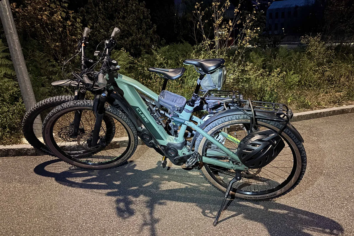 Zwei grüne E-Bikes mit Helmen sind nachts am Straßenrand geparkt. Sie stehen unter einer Laterne, die das Bild beleuchtet.