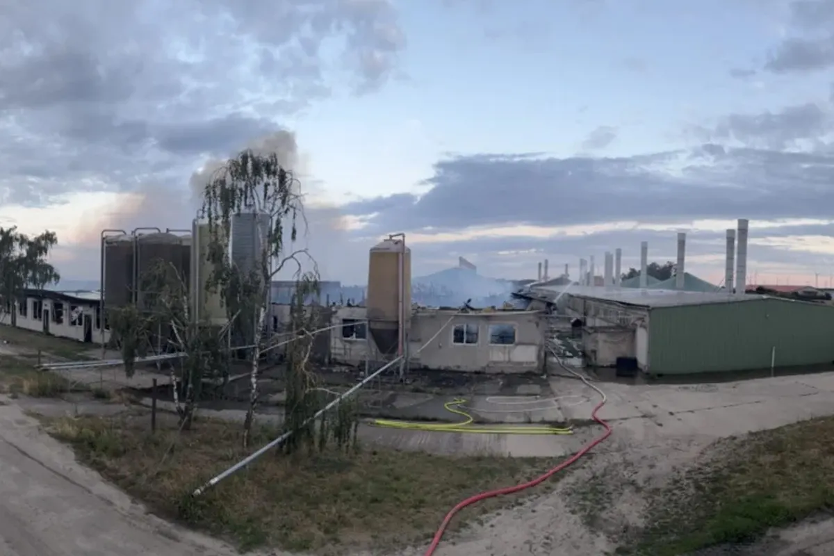 Die zerstörten Gebäude einer Industrieanlage sind zu sehen, mit Rauch, der aus dem Gelände aufsteigt. Der Himmel ist bedeckt und es sind Schläuche auf dem Boden verteilt.