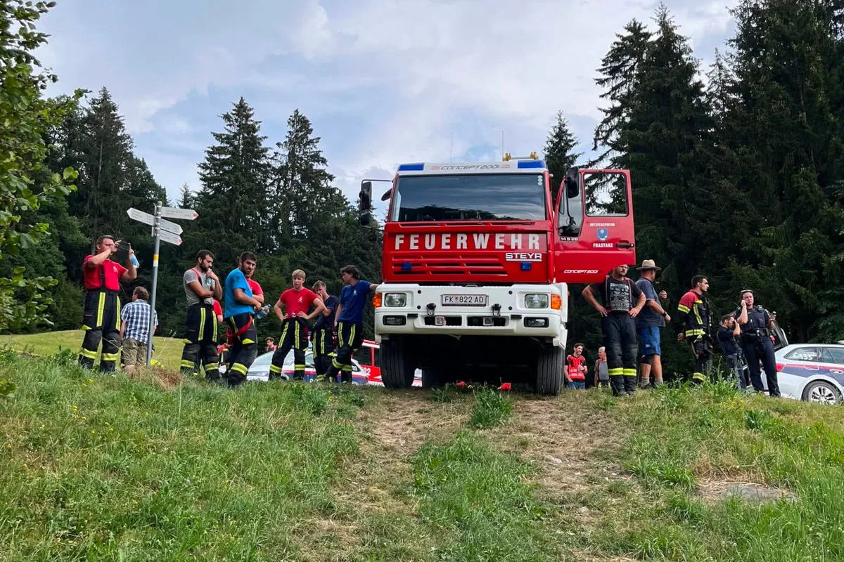 Ein rotes Feuerwehrfahrzeug steht auf einer Wiese, umgeben von Feuerwehrleuten in Uniformen. Sie scheinen sich abzustimmen.