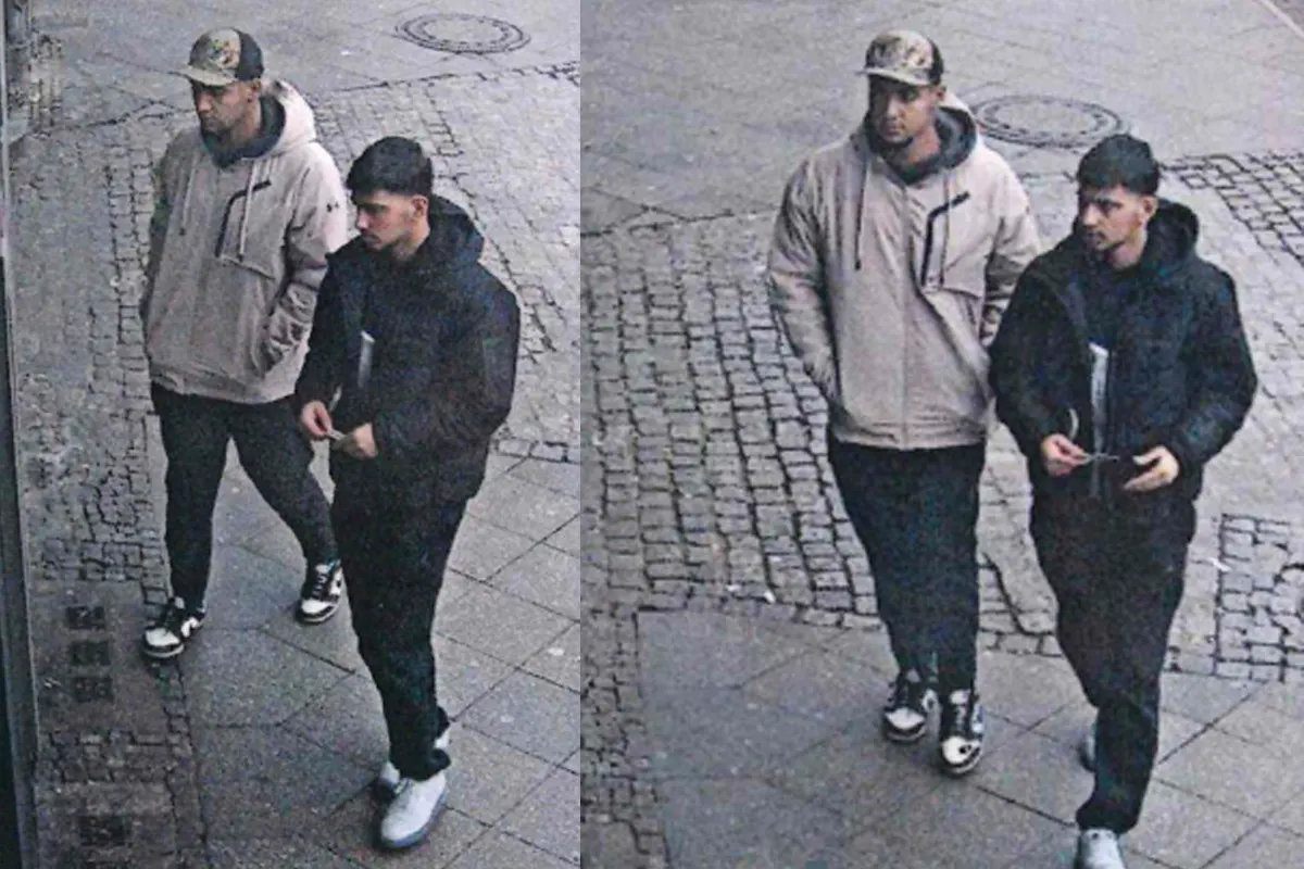 Zwei Männer laufen auf einem Gehweg; beide tragen dunkle Kleidung und einer eine Basecap.
