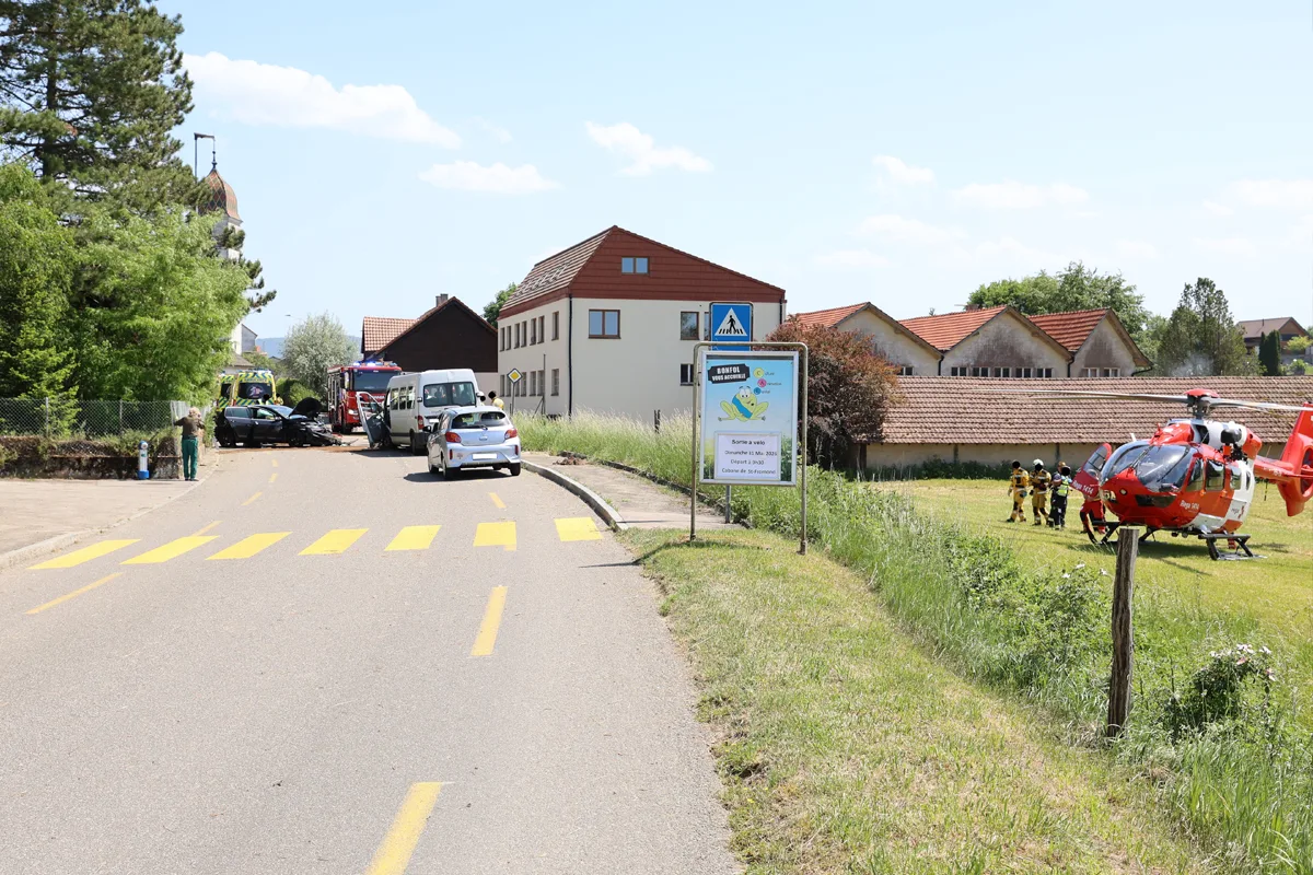 Ein Hubschrauber steht auf einer Wiese neben einer Straße, wo mehrere Fahrzeuge und Einsatzkräfte sichtbar sind.