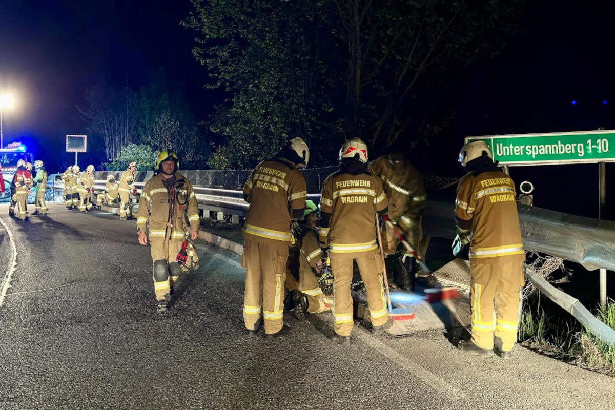 Mehrere Feuerwehrleute in Uniform stehen bei Nacht auf einer Autobahn neben einem beschädigten Leitplankenabschnitt. Ein Einsatzfahrzeug mit Blaulicht ist im Hintergrund sichtbar.