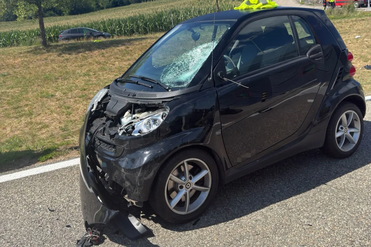 Ein schwarzer Kleinwagen ist am Straßenrand geparkt mit deutlichem Frontschaden und eingeschlagener Windschutzscheibe.