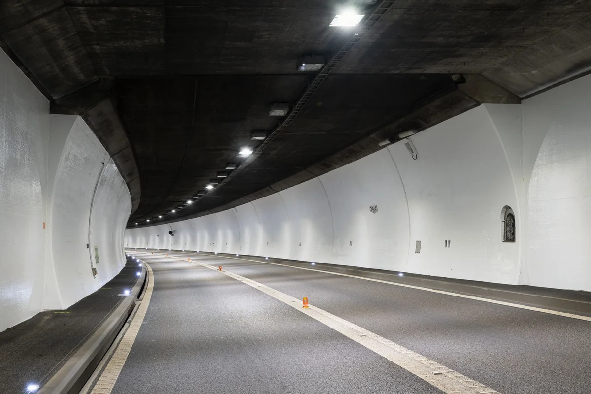 Ein leerer Straßentunnel, gleichmäßig beleuchtet, mit zentrierten Fahrstreifen, keine Fahrzeuge sichtbar.