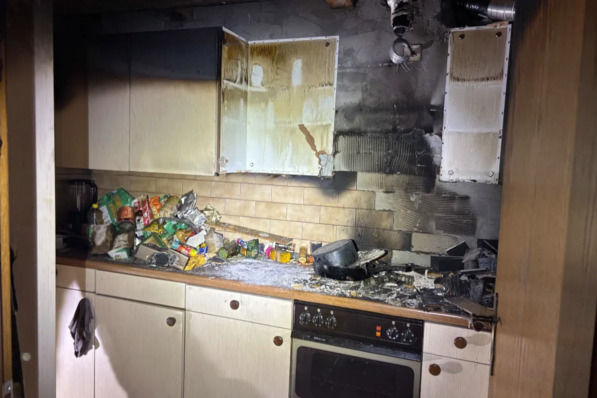 Ein Küchenschrank mit sichtbaren Brandschäden, verkohlten Oberflächen, und verstreute Lebensmittel auf der Arbeitsplatte.