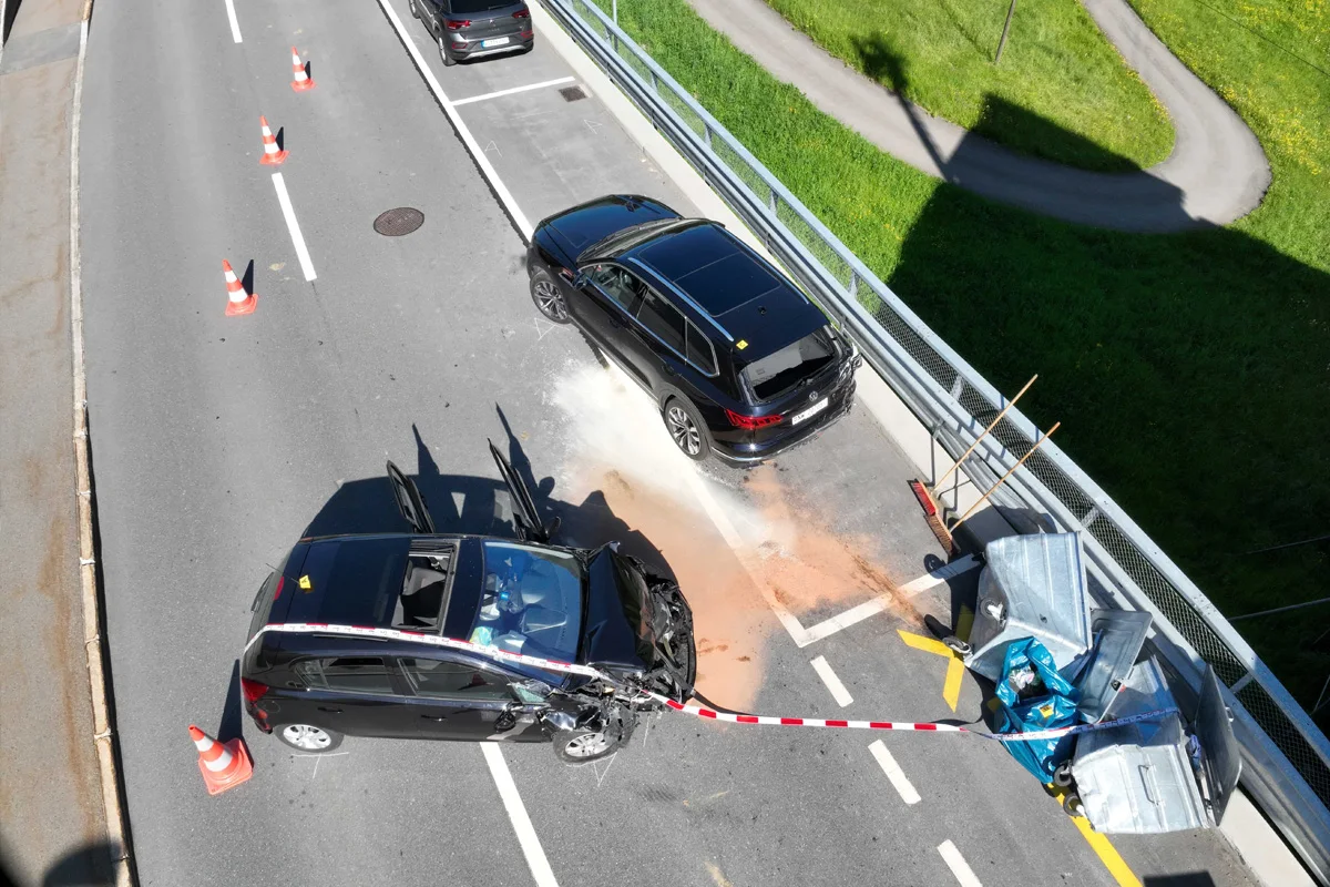 Ein Unfall auf einer Brücke zeigt zwei beschädigte Fahrzeuge, eines davon stark beschädigt, umgeben von Verkehrskegeln und Absperrband.